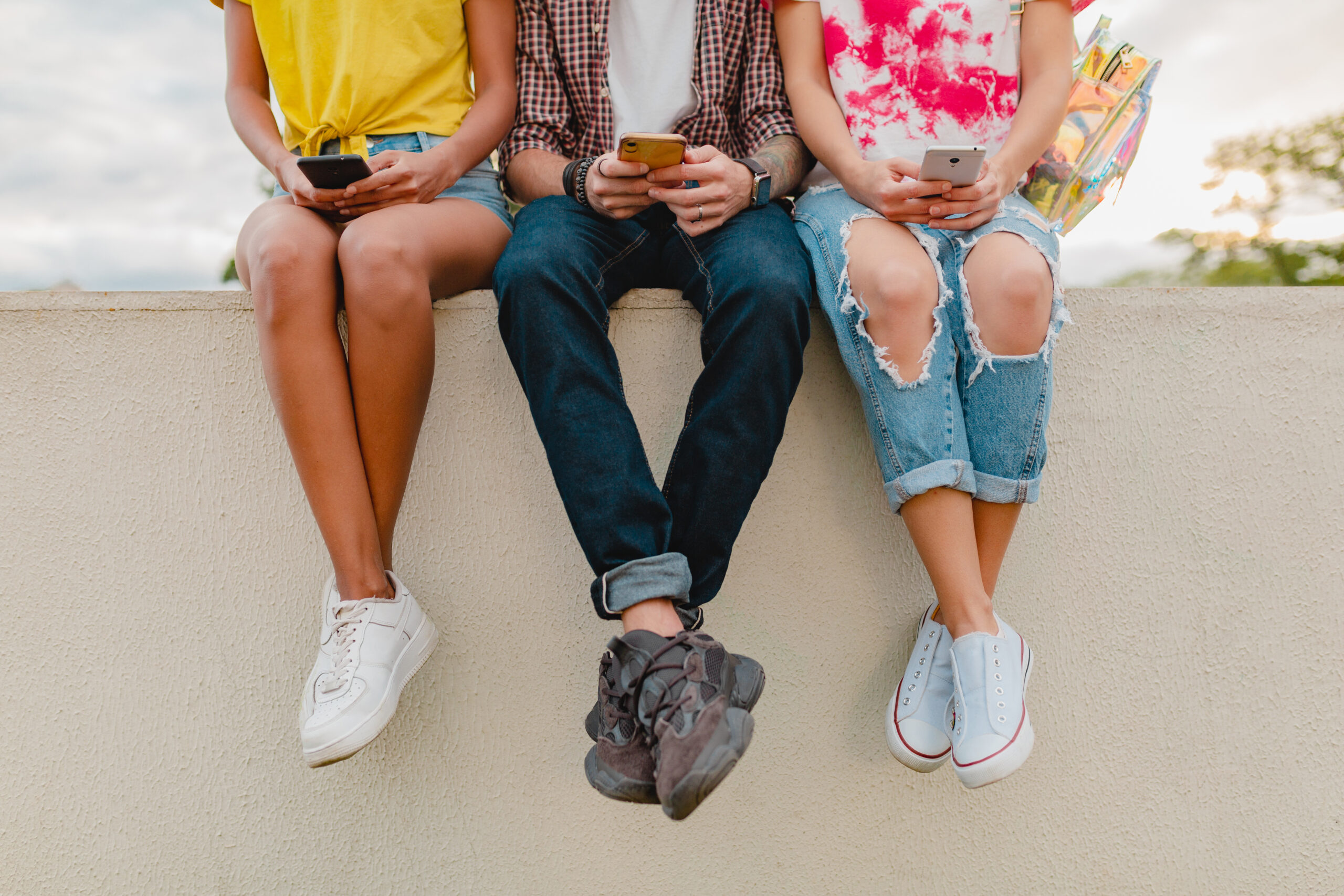 legs sneakers young company friends sitting park using smartphones scaled